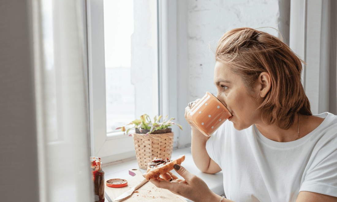 Person sitzt morgens am Fenster mit einer Tasse Tee oder Kaffee im natürlichen Morgenlicht.